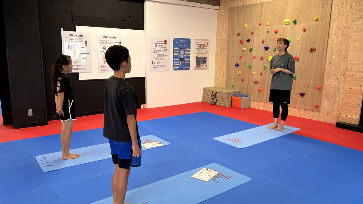 TAIJIKU 関内・桜木町校のジュニアアスリート体験会で、マットの上に立つ小学生と、正面から見ている石井愛トレーナー