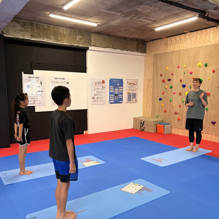 TAIJIKU 関内・桜木町校のジュニアアスリート体験会で、マットの上に立つ小学生と、正面から見ている石井愛トレーナー