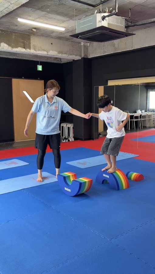 バランス器具の上に立つ子どもの手を取りながら、石井愛が身体の使い方を伝えている様子