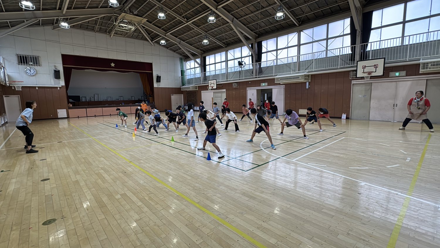 体育館いっぱいに広がった子どもたちが、低い姿勢で構える動きに取り組んでいる様子