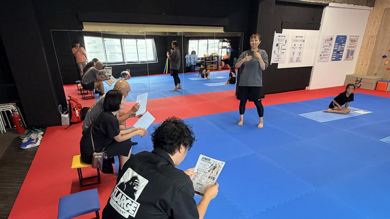 スタジオの後方で保護者が座って見学するなか、トレーナーが説明しているジュニアアスリート体験会の様子